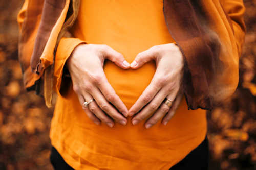 Pregnant woman holding hands in a heart shape over her tummy Pregnant woman holding hands in a heart shape over her tummy